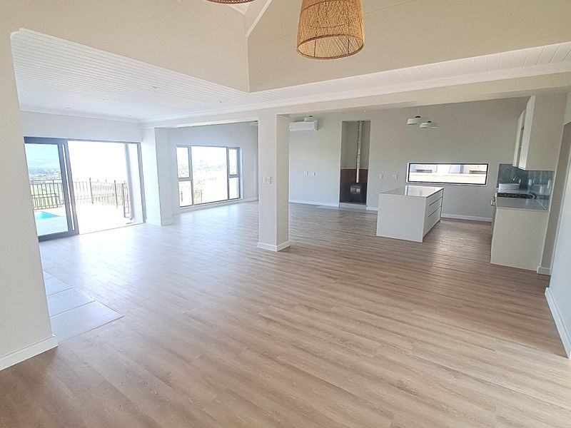 Spacious open-plan living area featuring a modern kitchen island, vaulted ceilings, built-in fireplace, and seamless access to an outdoor patio with scenic views.
