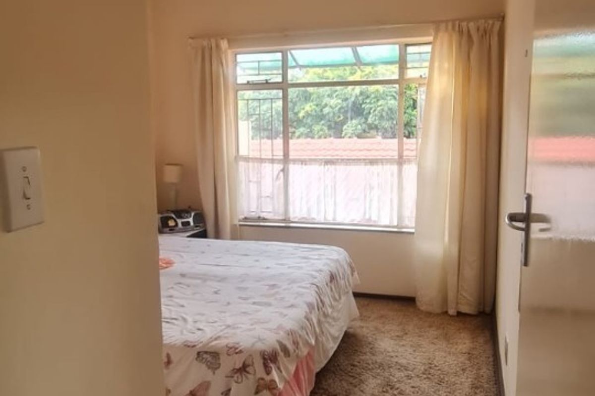 A standard bedroom featuring carpeted flooring, a large window allowing natural light, and neutral wall finishes.
