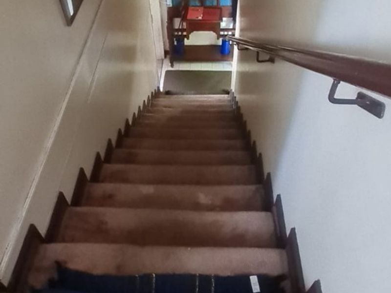 A narrow interior staircase featuring carpeted steps and a wooden handrail, leading down to a lower level landing area.