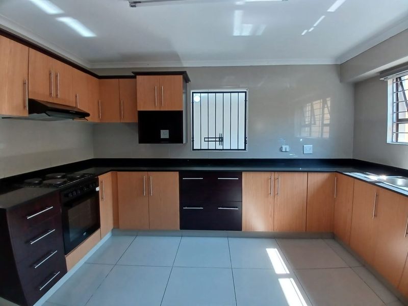 A clean, modern kitchen featuring two-tone built-in cabinetry, granite countertops, integrated oven and hob, and tiled flooring with security bars on the windows.