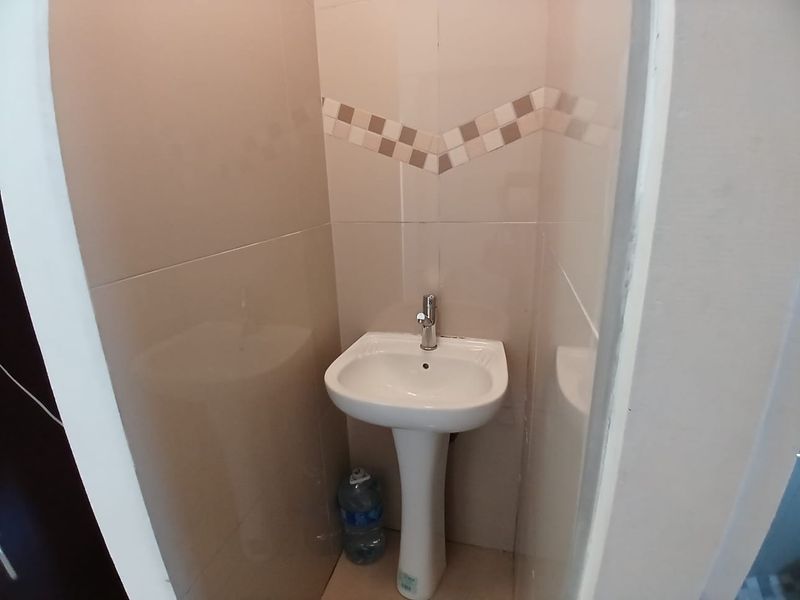 A compact guest bathroom or powder room featuring a white pedestal basin with a chrome mixer tap and neutral ceramic wall tiling.