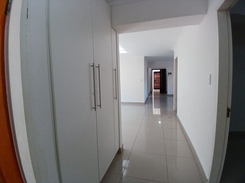 A bright, empty hallway featuring neutral tiled flooring and built-in storage cupboards, leading towards the main entrance of the apartment.