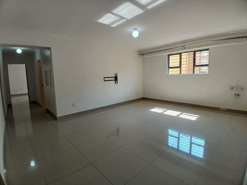 A bright, spacious, and empty living area featuring neutral tiled flooring and large windows, providing a clean canvas for interior design.