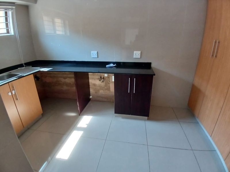 A compact kitchen featuring granite countertops, tiled flooring, and built-in cabinetry, currently requiring repairs to the under-counter area and missing cabinet components.