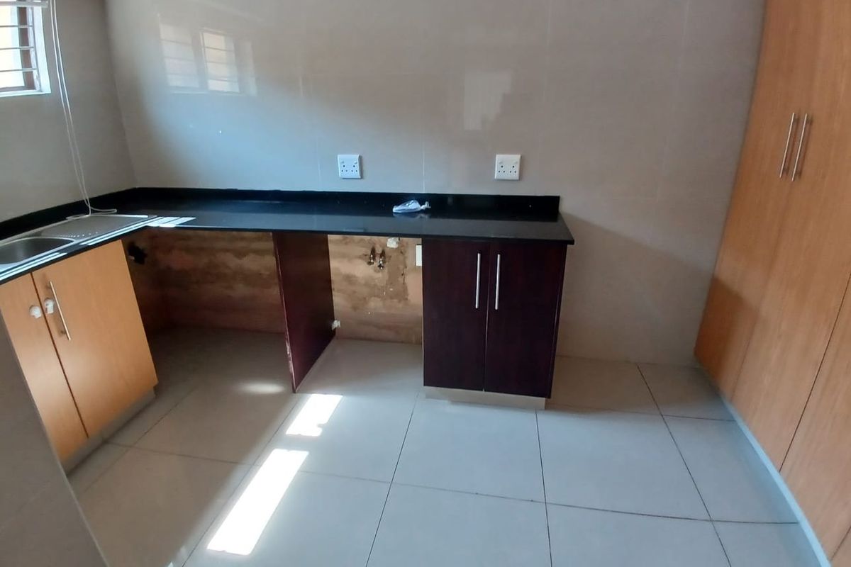 A compact kitchen featuring granite countertops, tiled flooring, and built-in cabinetry, currently requiring repairs to the under-counter area and missing cabinet components.