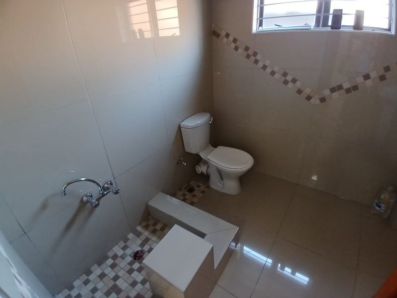 A functional bathroom featuring tiled walls and flooring, a standard toilet, and a shower area with wall-mounted faucet.