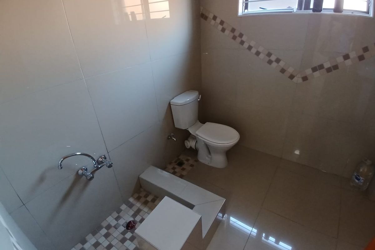 A functional bathroom featuring tiled walls and flooring, a standard toilet, and a shower area with wall-mounted faucet.