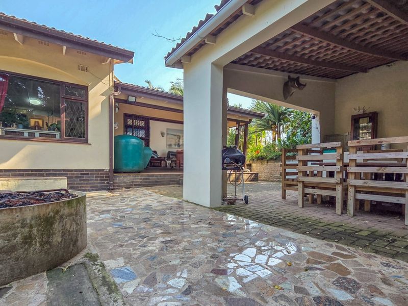 Spacious covered patio area featuring a built-in fire pit, brick and stone paving, and a timber pergola, ideal for outdoor entertaining.