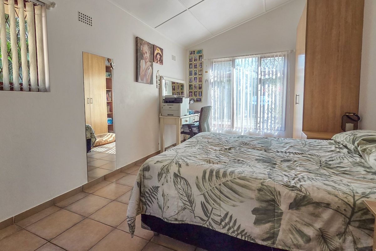 A bedroom featuring tiled flooring, a vaulted ceiling, and built-in wardrobe storage, with natural light provided by large windows with security bars.