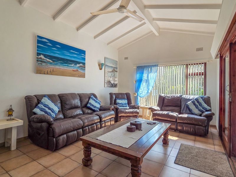 Spacious living room featuring a vaulted ceiling with exposed beams, ceiling fan, ceramic tile flooring, and large sliding glass doors providing natural light.