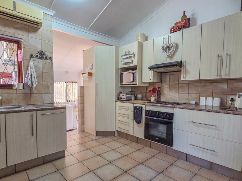 A functional kitchen featuring light-toned cabinetry, tiled flooring, a built-in oven with hob, and a double sink with a tiled backsplash.