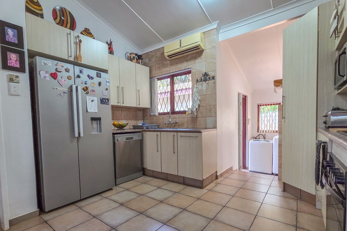 A functional kitchen featuring tiled flooring, built-in cabinetry, a tiled backsplash, and an integrated air conditioning unit, with an adjacent laundry area visible.