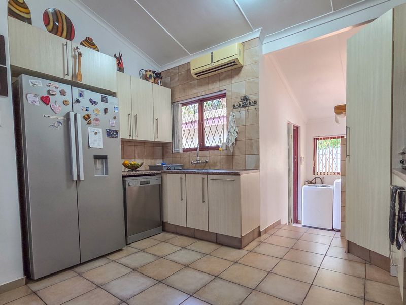 A functional kitchen featuring tiled flooring, built-in cabinetry, a tiled backsplash, and an integrated air conditioning unit, with an adjacent laundry area visible.