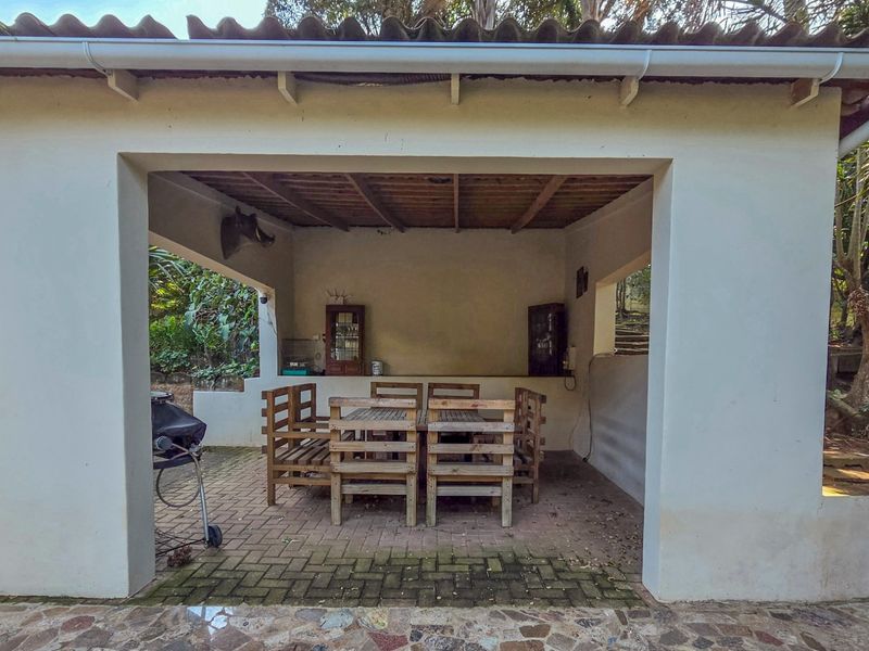 A covered outdoor patio area featuring exposed timber beam ceilings, brick paving, and a built-in masonry counter, ideal for outdoor entertaining.