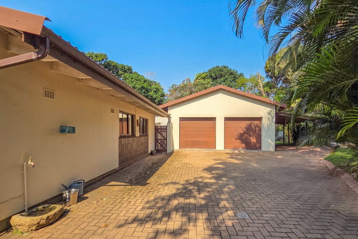 A view of the rear exterior featuring a paved driveway leading to a double garage with roll-up doors and surrounding garden area.