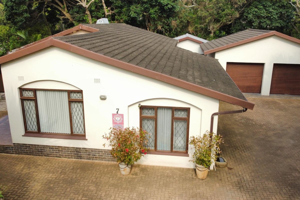 Aerial view of the property featuring a tiled roof, brick paved driveway, and a double garage with roller doors.