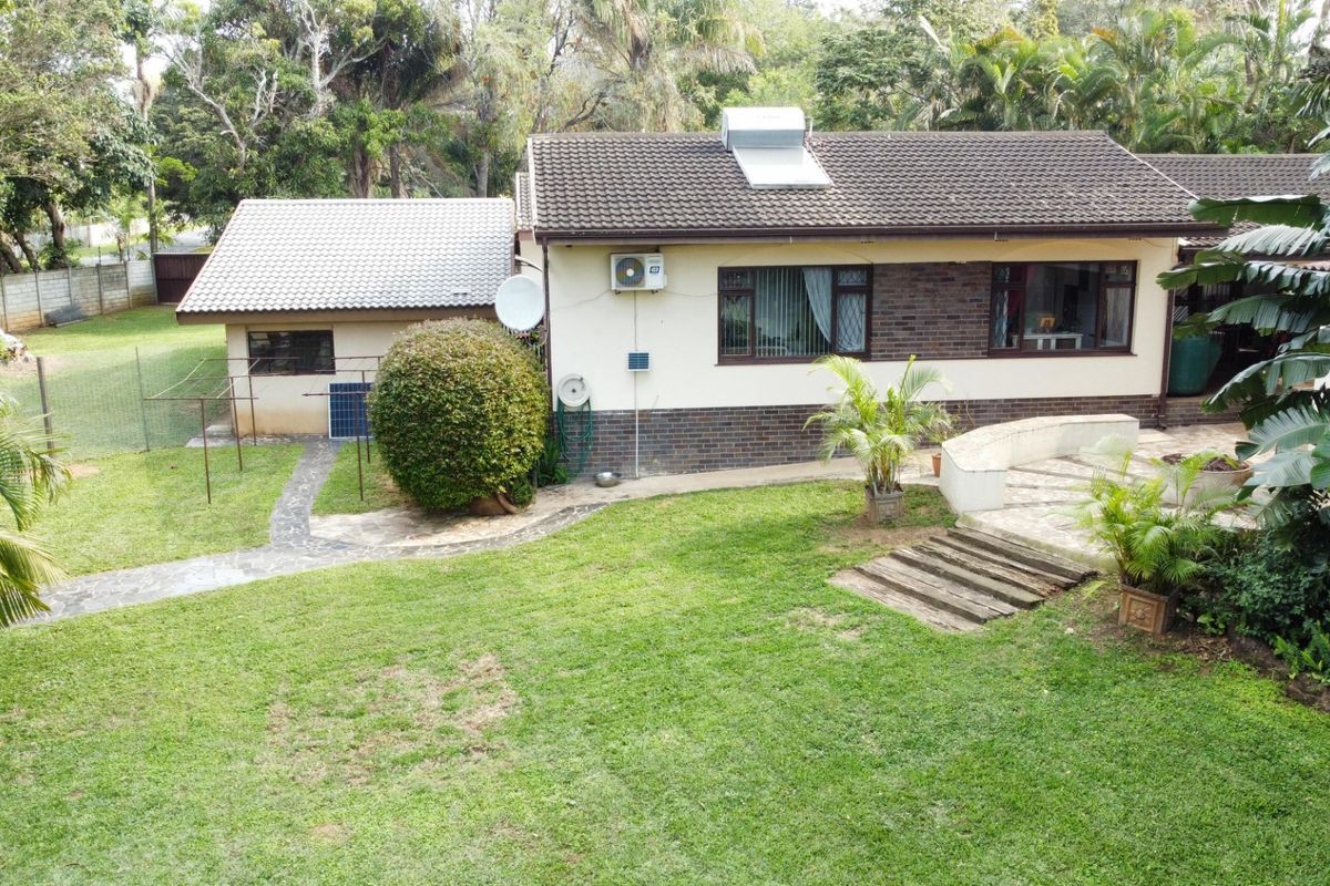 Rear view of the house featuring a tiled roof with solar water heater, brick and plaster facade, and a landscaped garden with paved pathways.