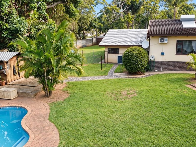 Spacious rear garden featuring a swimming pool, paved patio area, established lawn, and a detached garden shed.