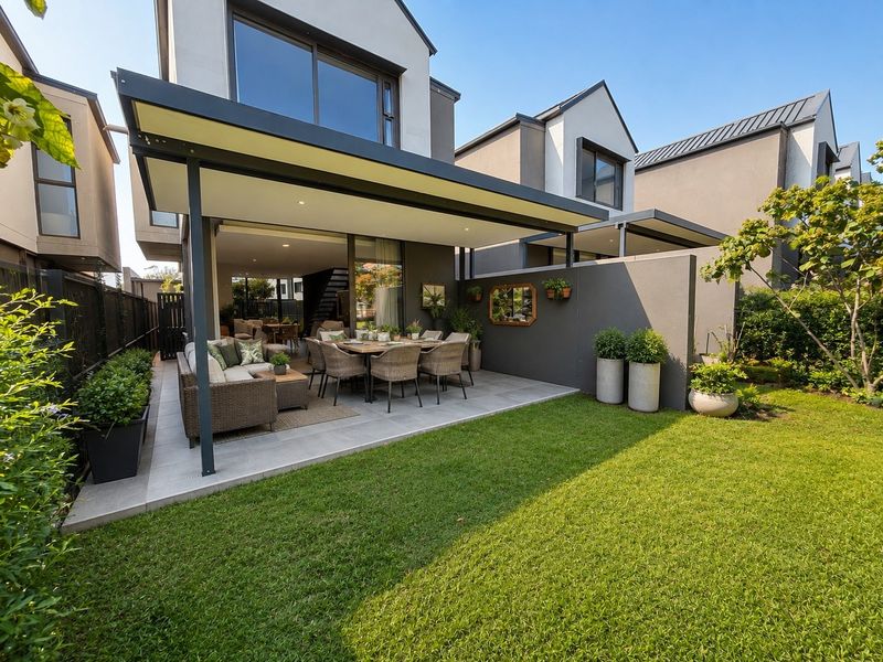 A modern covered patio area featuring tiled flooring and recessed lighting, seamlessly connecting to the interior living space and overlooking a private garden.