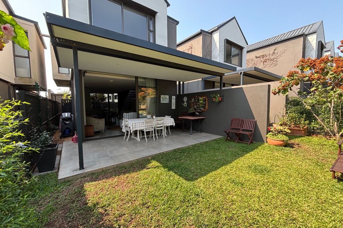 Rear view of the townhouse featuring a covered patio with tiled flooring, sliding glass doors, and a private garden area.
