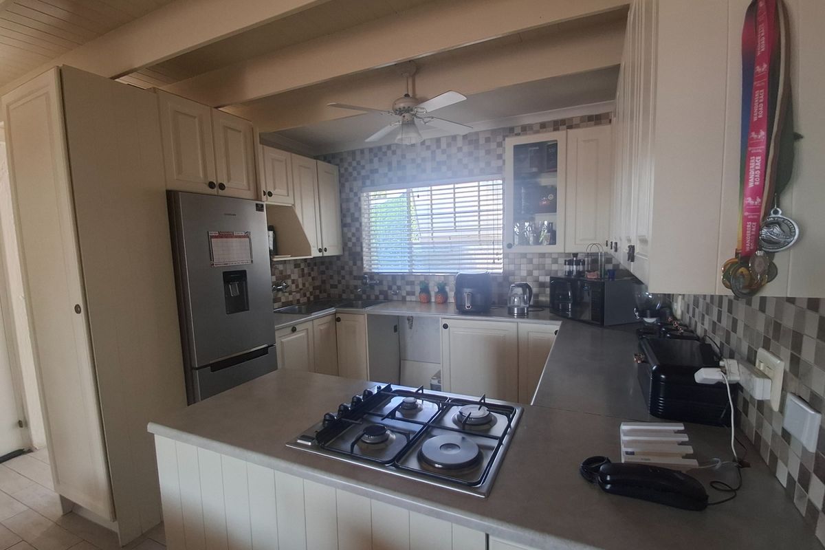 A functional kitchen featuring a gas cooktop, tiled backsplash, and ample built-in cabinetry with an exposed beam ceiling.