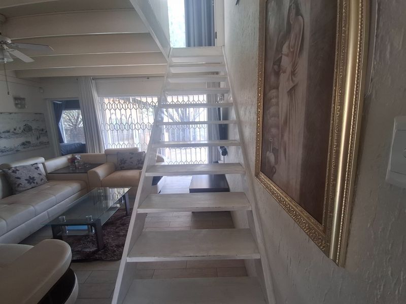 Living area featuring tiled flooring, a ceiling fan, and a central staircase leading to an upper level with security gate access.