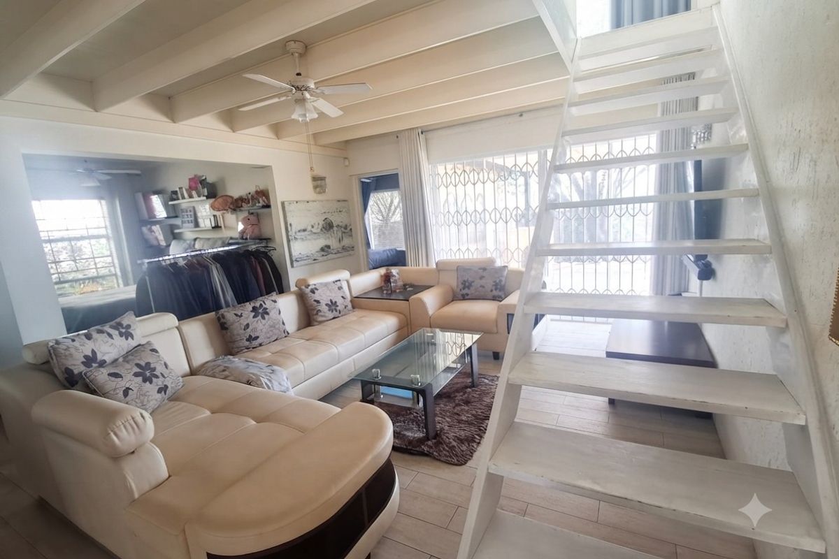 Open-plan living area featuring exposed timber ceiling beams, a central staircase, and tiled flooring with access to a secure patio area.