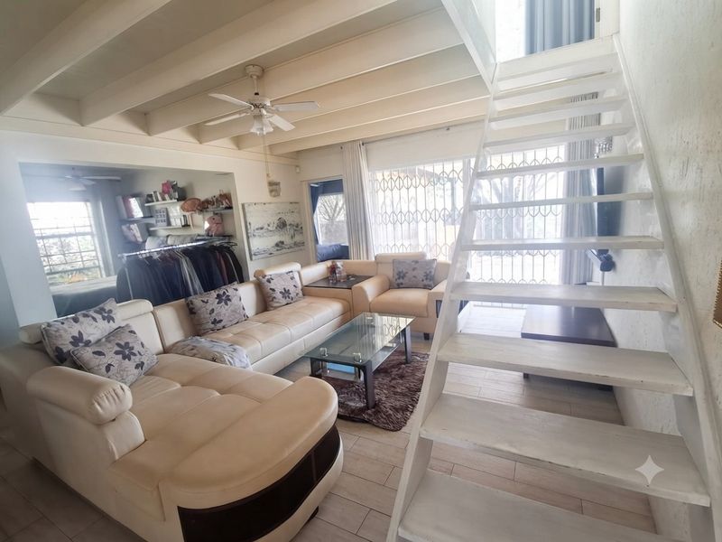 Open-plan living area featuring exposed timber ceiling beams, a central staircase, and tiled flooring with access to a secure patio area.