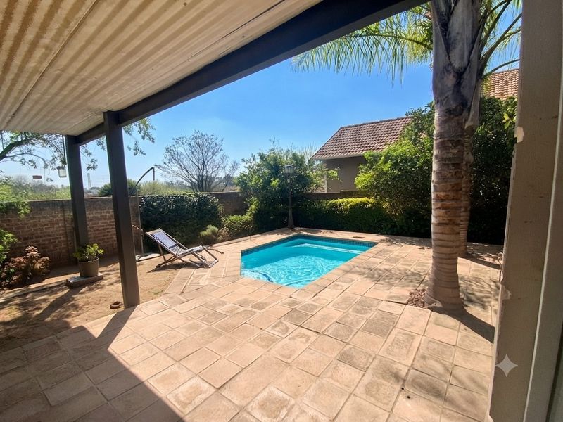 Outdoor entertainment area featuring a covered patio, tiled flooring, and a private swimming pool set within a landscaped garden.