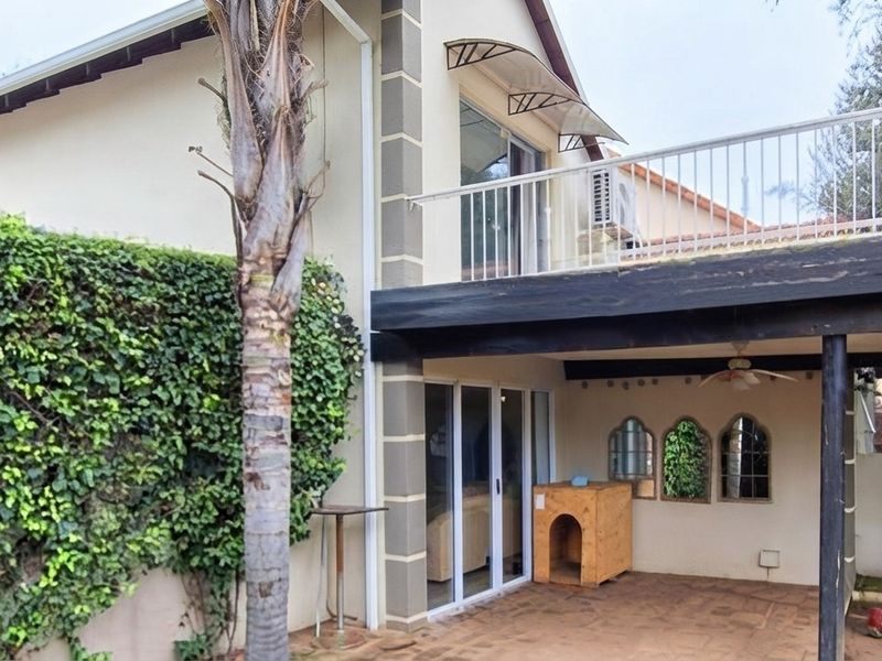 Rear view of the property featuring a covered patio area, an upper-level balcony with metal railing, and sliding glass doors leading into the home.