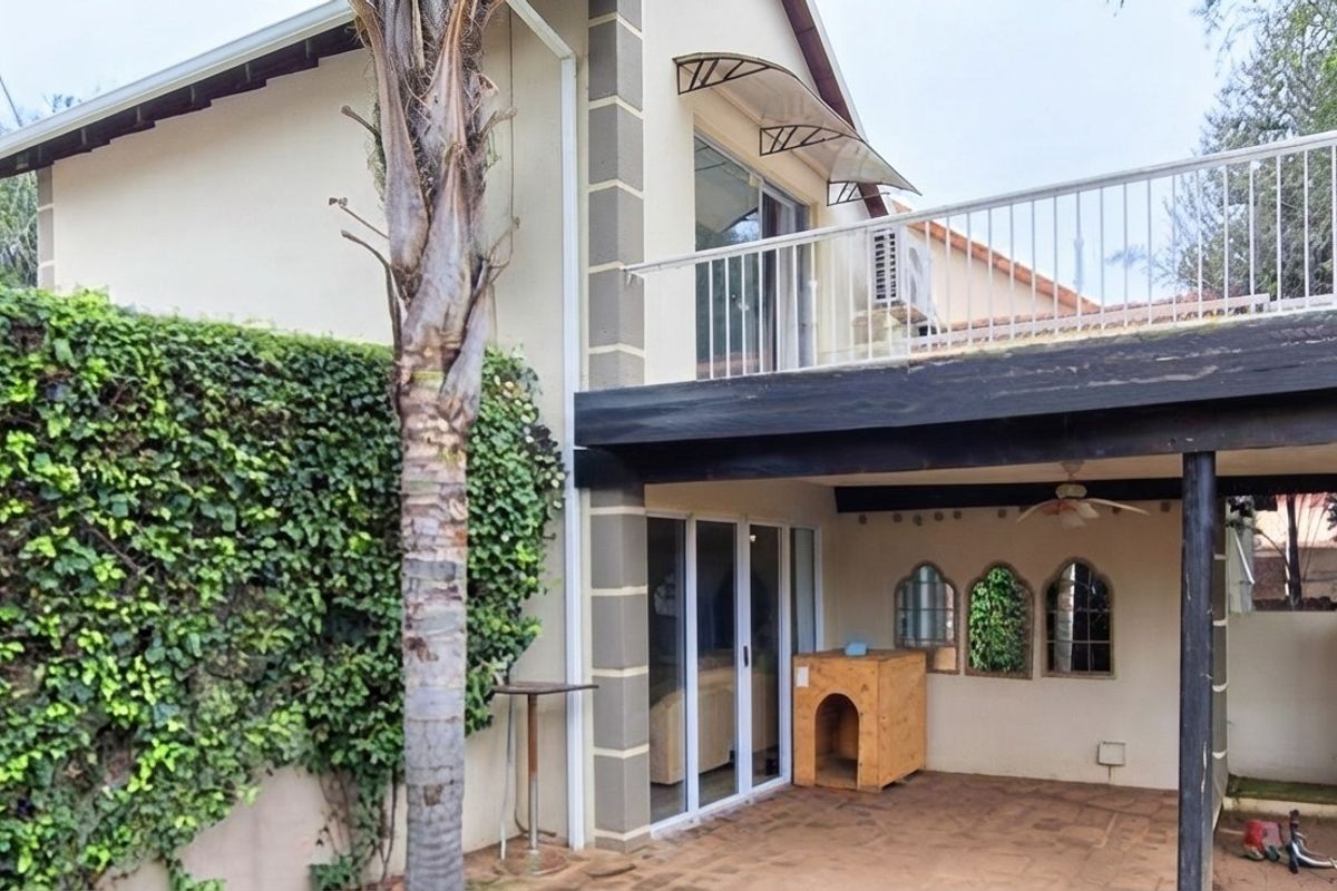 Rear view of the property featuring a covered patio area, an upper-level balcony with metal railing, and sliding glass doors leading into the home.
