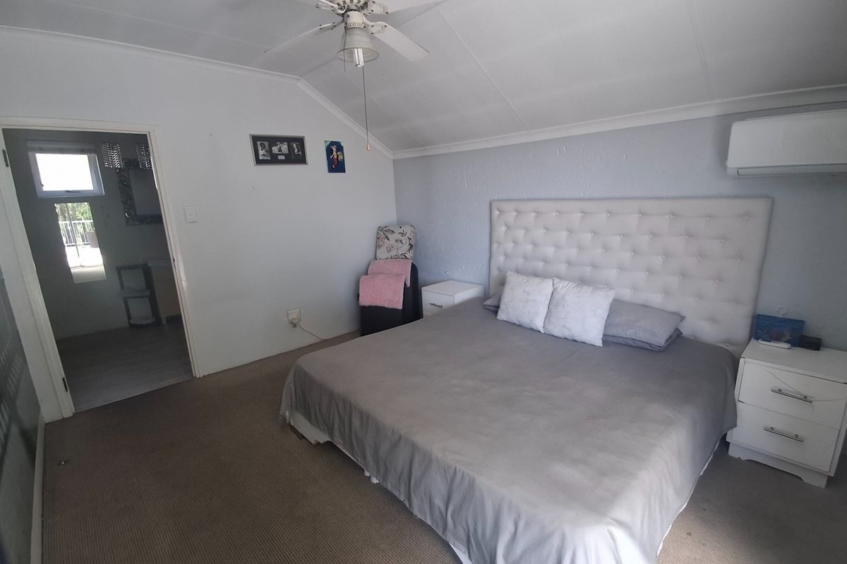 A bedroom featuring a vaulted ceiling with a fan, split-system air conditioning, and carpeted flooring, with an adjoining bathroom visible through the doorway.