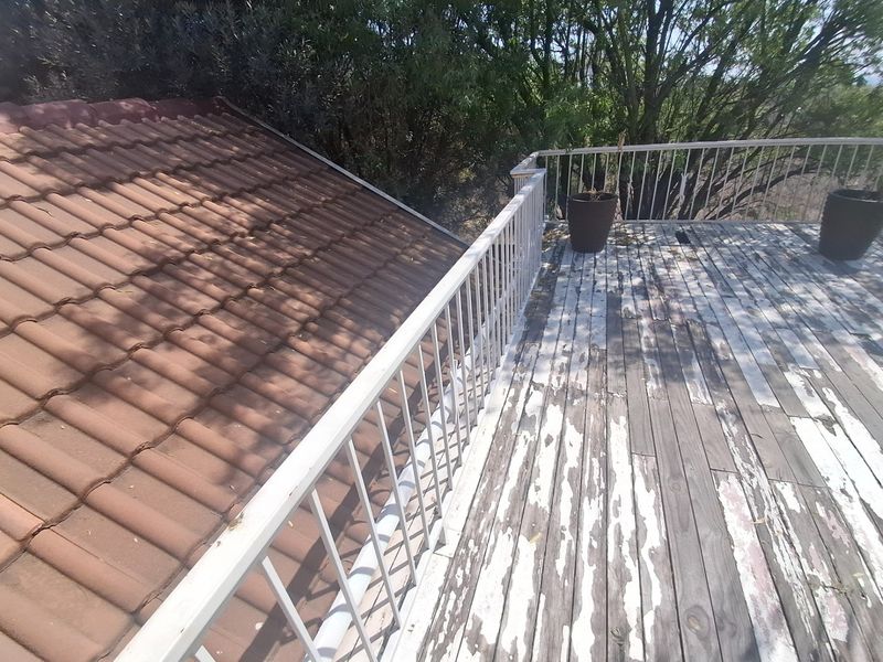 An elevated outdoor balcony featuring a metal balustrade and weathered timber decking, adjacent to a tiled roof section.