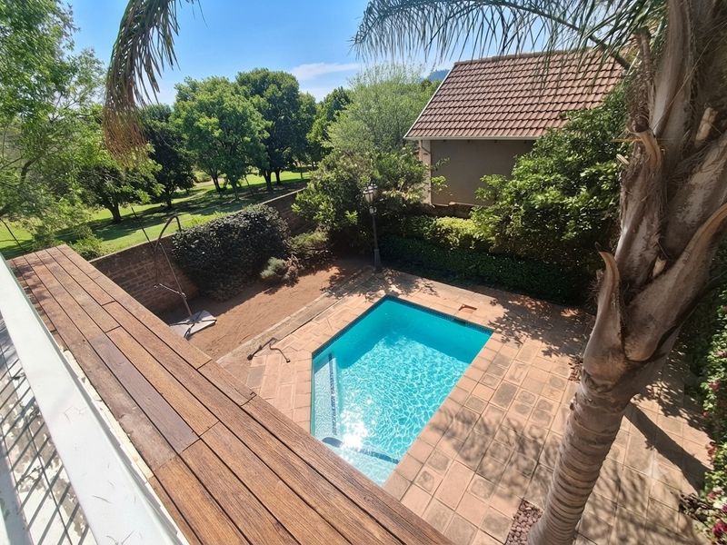 An elevated view of a private swimming pool with a tiled surround, adjacent wooden deck, and established garden area.