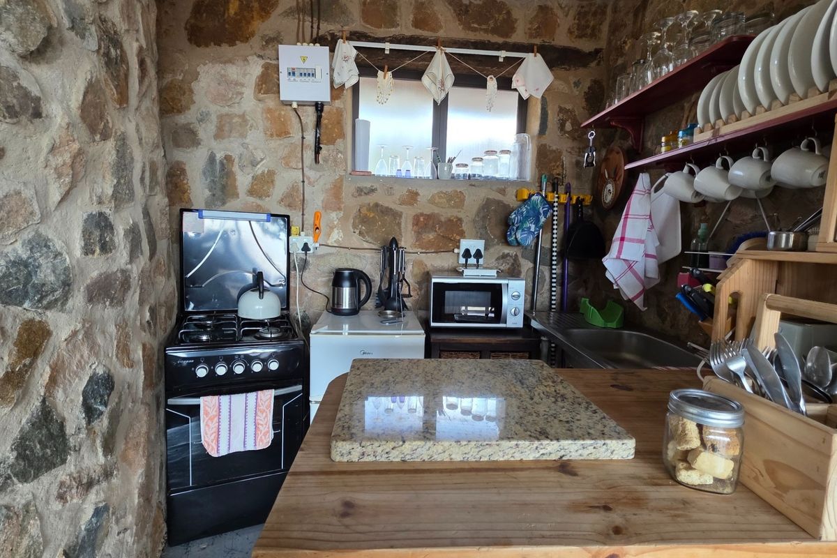 A rustic kitchen area featuring exposed stone walls, a gas stove, and a compact stainless steel sink with open shelving.