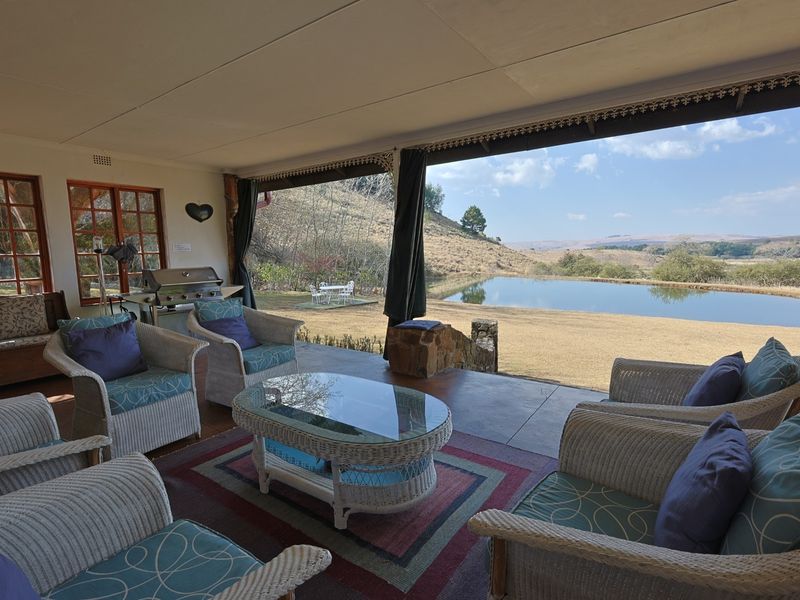 A spacious covered patio featuring concrete flooring and timber-framed windows, offering expansive views of the surrounding farm landscape and private dam.