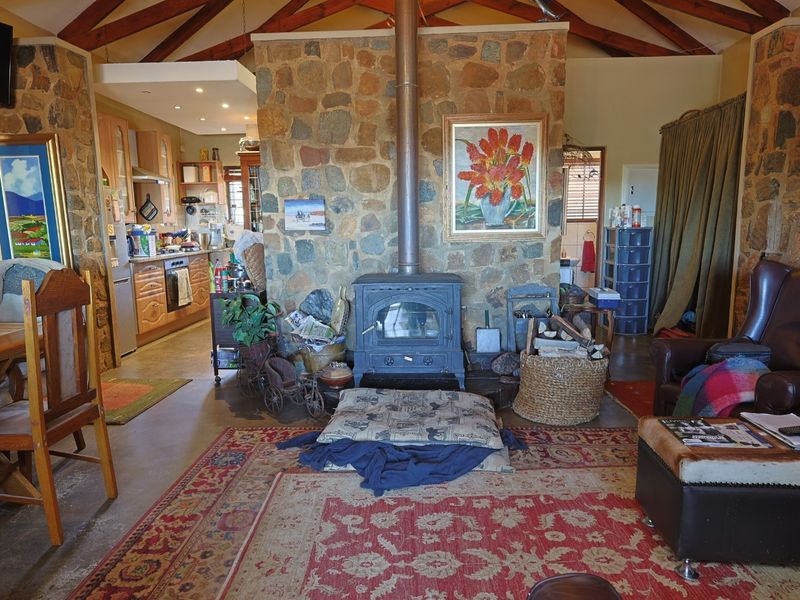 Open-plan living area featuring a prominent stone fireplace with a wood-burning stove, exposed timber rafters, and an adjoining kitchen with fitted cabinetry.