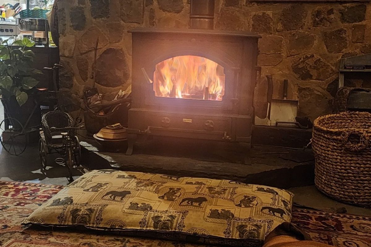 Cozy living area featuring a rustic stone wall and a functional cast iron wood burning stove set on a raised stone hearth.