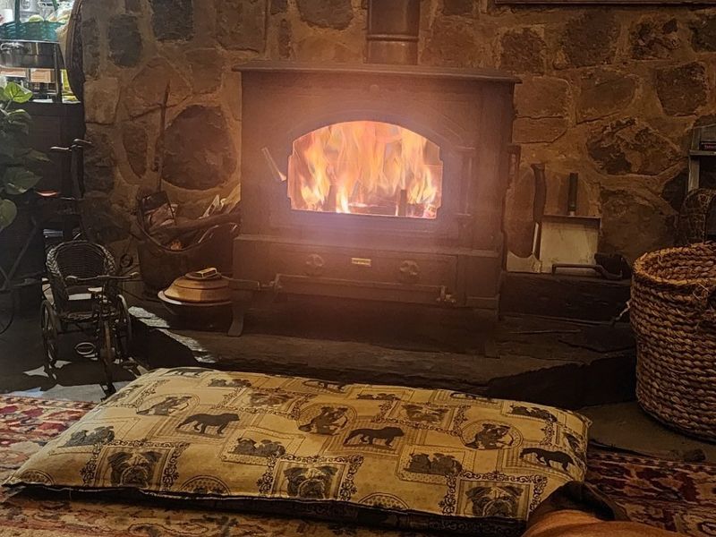 Cozy living area featuring a rustic stone wall and a functional cast iron wood burning stove set on a raised stone hearth.