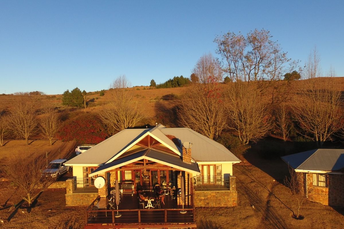 Aerial view of a farm-style residence featuring a corrugated metal roof, stone cladding, and an expansive timber deck overlooking the surrounding landscape.