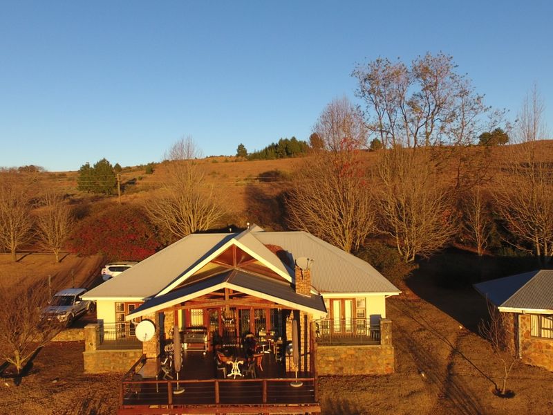 Aerial view of a farm-style residence featuring a corrugated metal roof, stone cladding, and an expansive timber deck overlooking the surrounding landscape.