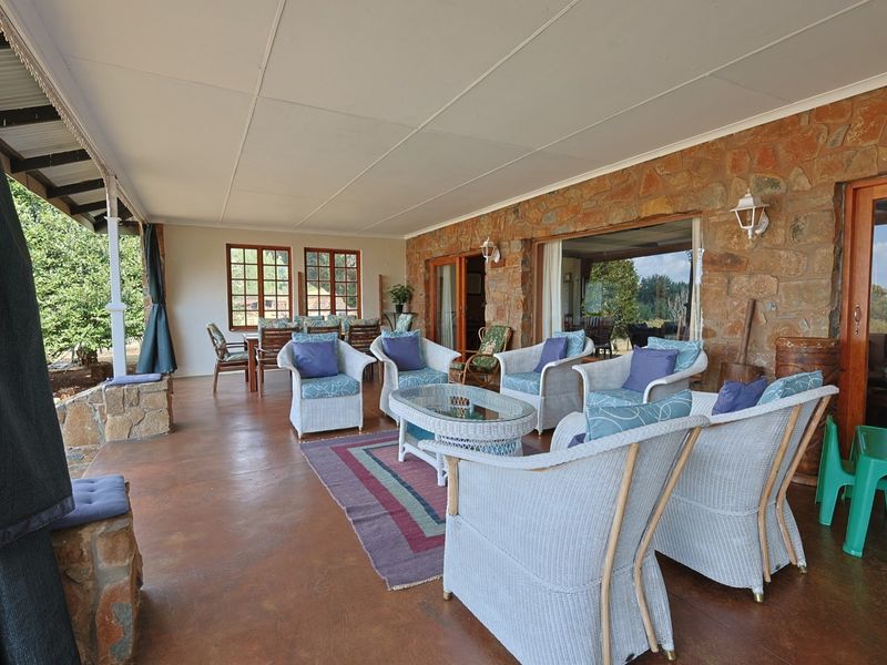 A spacious covered patio featuring rustic stone wall cladding, concrete flooring, and large sliding glass doors providing access to the interior living spaces.