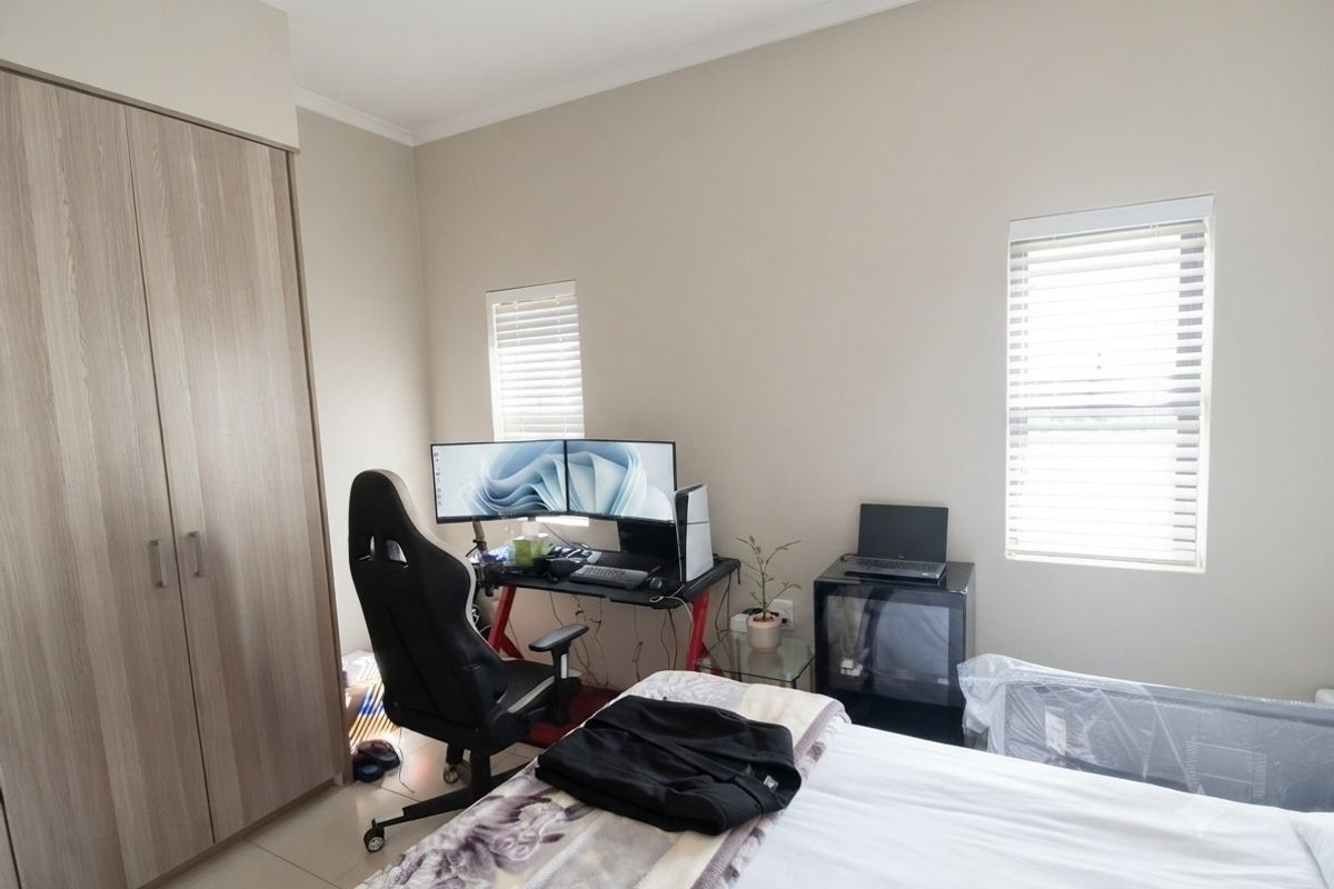 A functional bedroom featuring neutral walls, tiled flooring, built-in wardrobe storage, and dual windows with fitted venetian blinds.