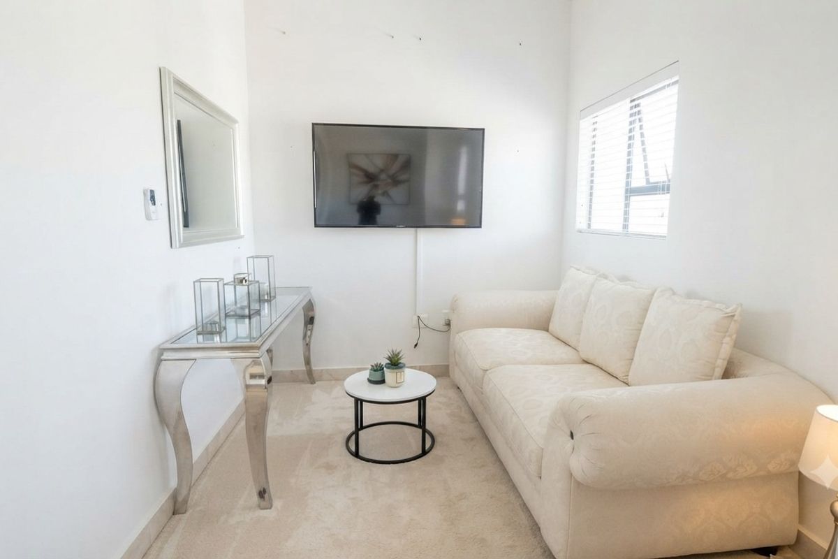 A compact living room featuring neutral carpeting, white walls, and a window with fitted venetian blinds.