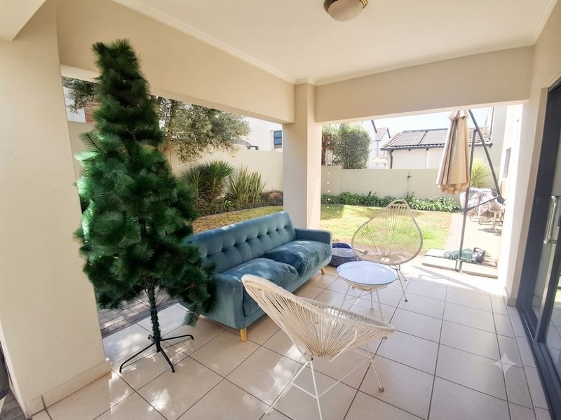 A covered outdoor patio area featuring tiled flooring and direct access to the rear garden, providing a functional space for outdoor relaxation.