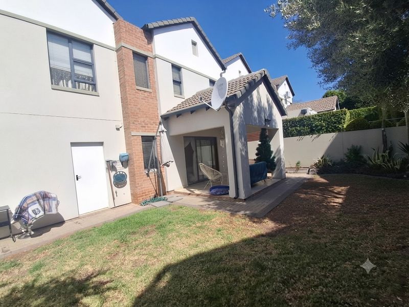 Rear view of the property featuring a covered patio area, brick paving, and a private garden with boundary walls.