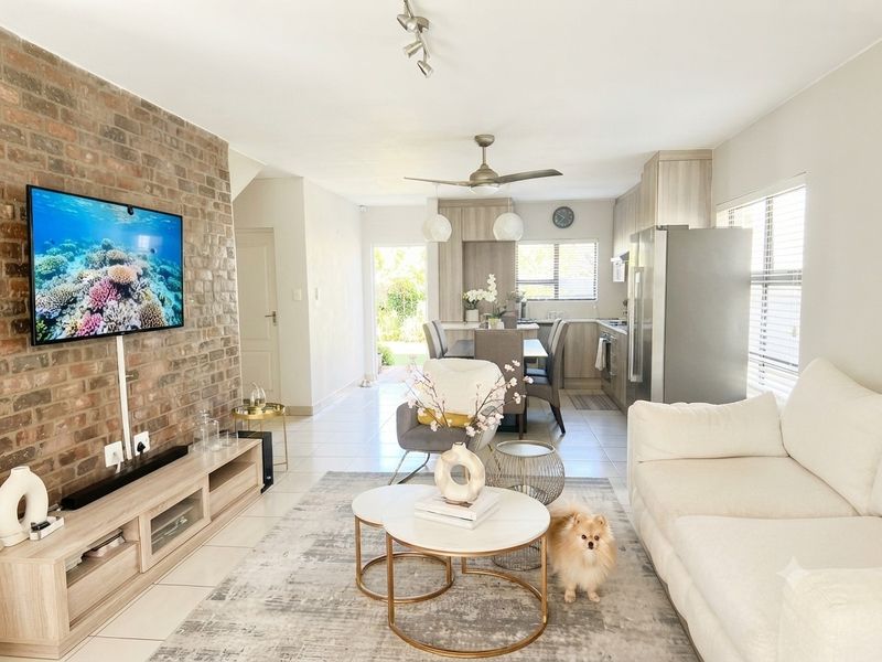 Bright open-plan living and kitchen area featuring an exposed brick wall, modern cabinetry, and tiled flooring with seamless flow to the rear garden.