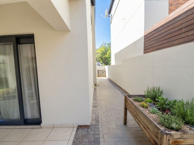 A clean side passage featuring paved flooring, a modern boundary wall, and access to the home via a sliding glass door.