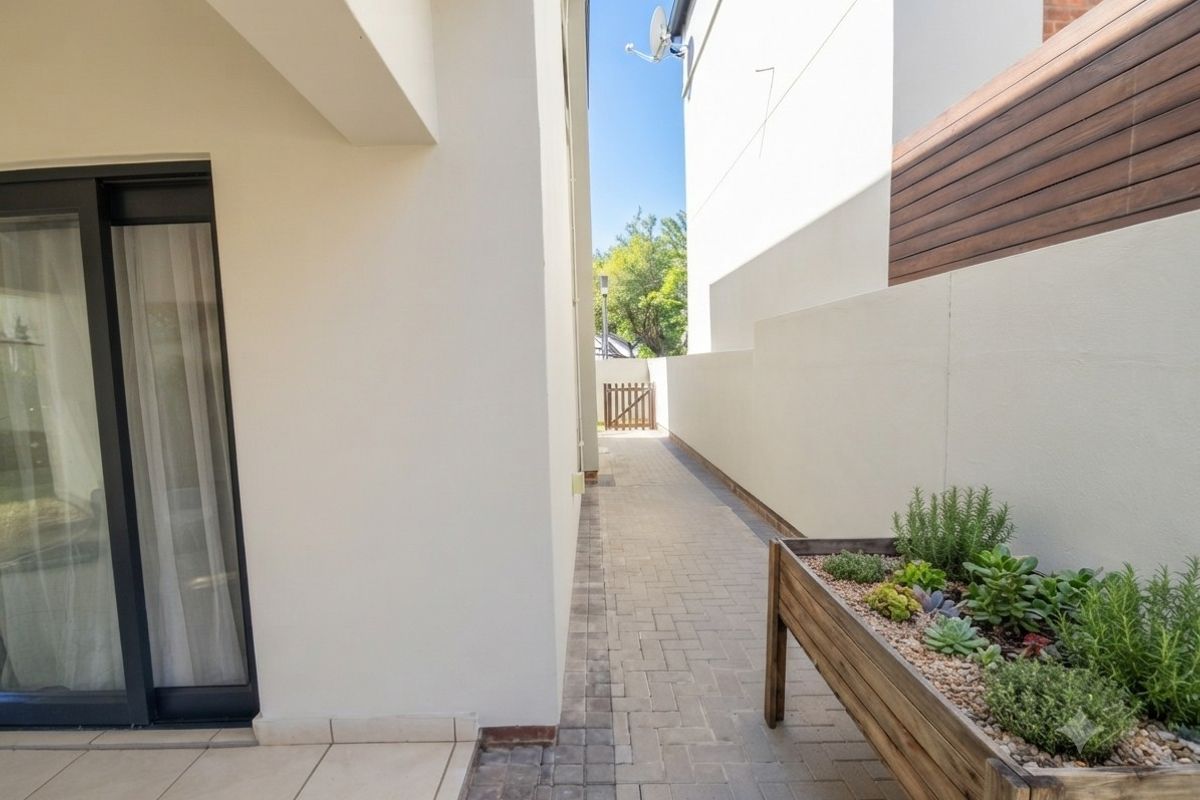 A clean side passage featuring paved flooring, a modern boundary wall, and access to the home via a sliding glass door.