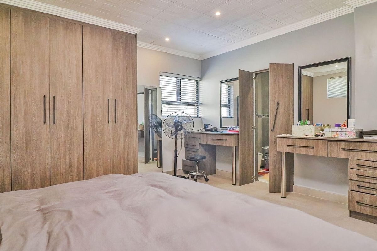 Spacious bedroom featuring extensive built-in cabinetry, a dedicated vanity area, tiled ceiling finishes, and integrated lighting with access to an en-suite bathroom.